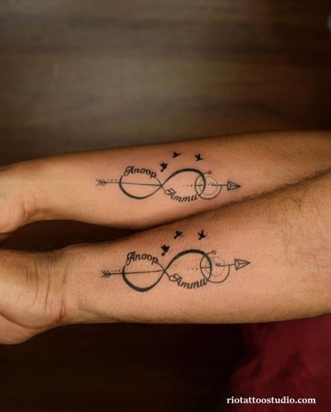 Matching couple name tattoos "Anoop" and "Ammu" with infinity symbol, arrow and birds on forearms, name tattoo ideas