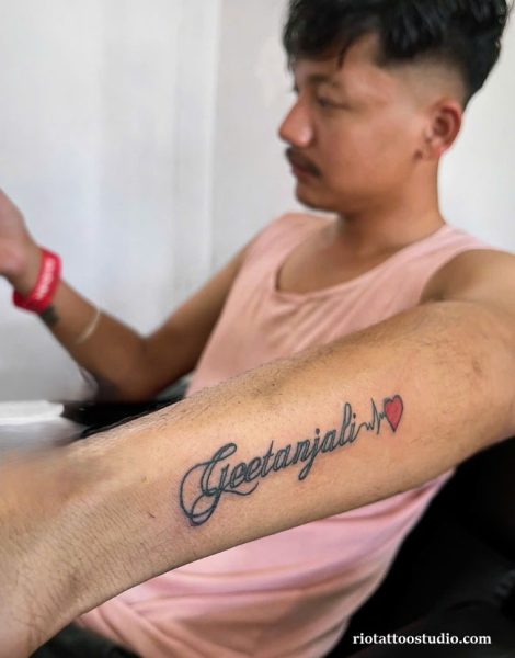 Name tattoo "Geetanjali" in cursive with heartbeat line and red heart on forearm, name tattoo ideas