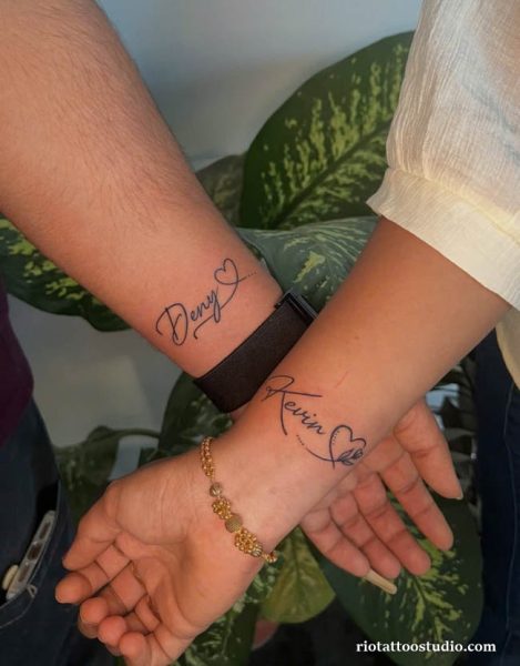 Matching couple name tattoos "Deny" and "Kevin" with hearts on wrists, name tattoo ideas