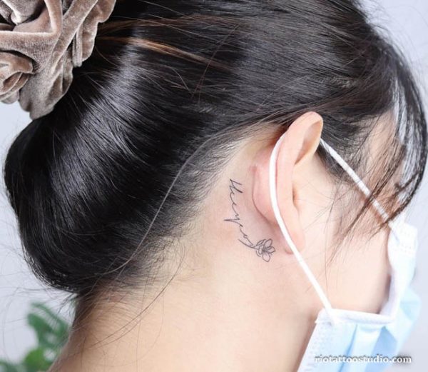 Delicate "Mom" name tattoo with small flower behind the ear on the neck, name tattoo ideas