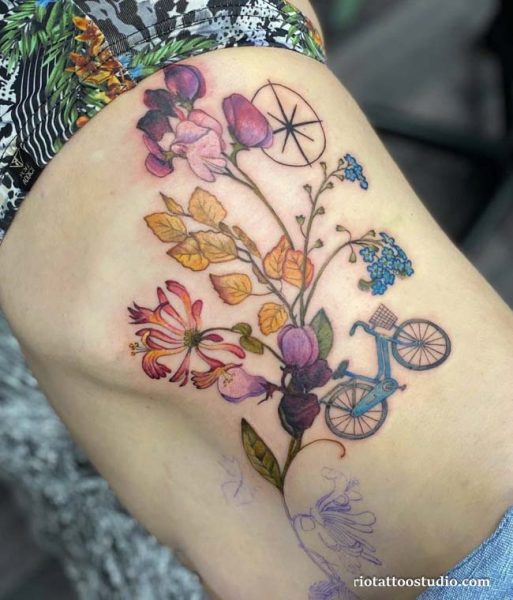 Colorful floral bouquet with bicycle and compass rib tattoo on woman’s hip, vibrant rib tattoo ideas