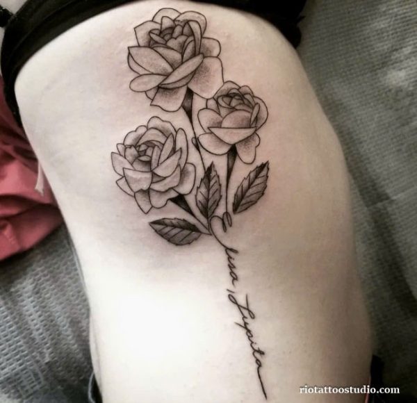 Black and grey realistic roses with script name rib tattoo on woman’s side, elegant rib tattoo ideas
