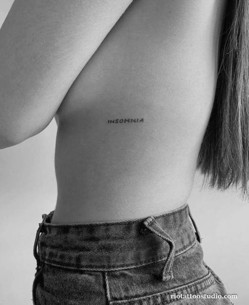 Minimalist single word “INSOMNIA” rib tattoo on woman’s side, simple text rib tattoo ideas