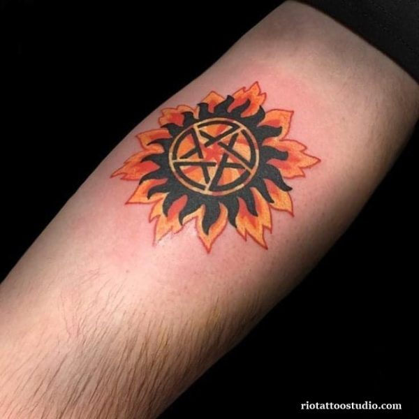 Flaming anti-demon supernatural tattoo with orange and black sunburst pentagram on forearm, supernatural tattoo ideas