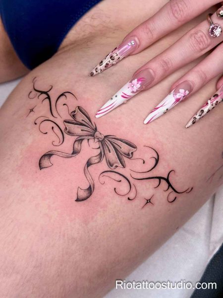 Elegant black bow ribbon thigh tattoo with flowing swirls and sparkles, thigh tattoo ideas