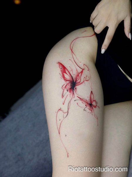 Red watercolor butterfly thigh tattoo with flowing ribbons and two butterflies on upper thigh, thigh tattoo ideas