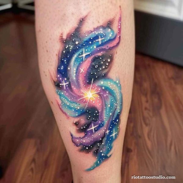 Full-color vibrant watercolor spiral galaxy tattoo on the back of the leg featuring deep blues, purples, and cosmic pinks with high-contrast white star clusters and splatters.