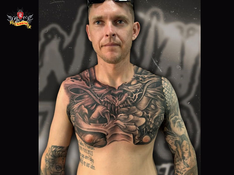 Black and white close-up of a powerful man showing a chest demon tattoo at Rio Tattoo Studio.