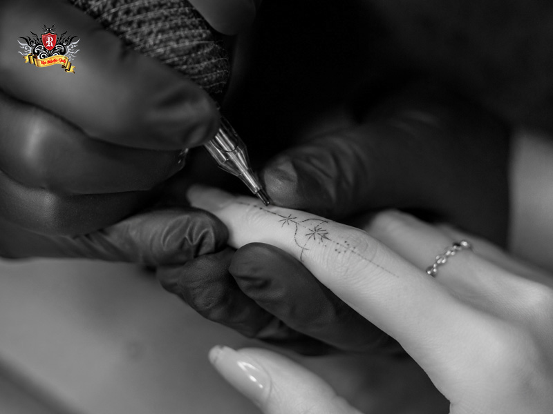 Artistic B&W photo of an artist carefully inking a precise finger tattoo for women at Rio Tattoo Studio.